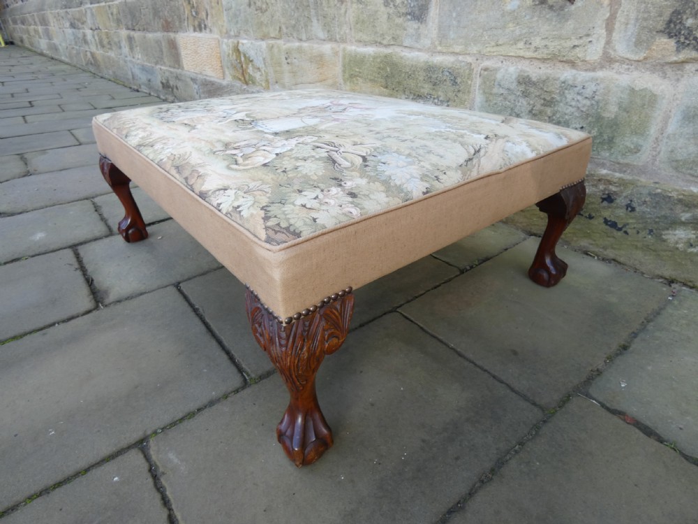 A large square upholstered centre stool featuring a tapestry top with figures in a landscape and dark carved mahogany cabriole legs with ball and claw feet. View V