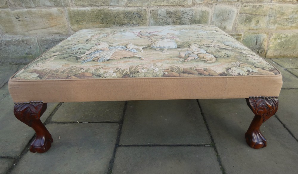 A large square upholstered centre stool featuring a tapestry top with figures in a landscape and dark carved mahogany cabriole legs with ball and claw feet. View VI