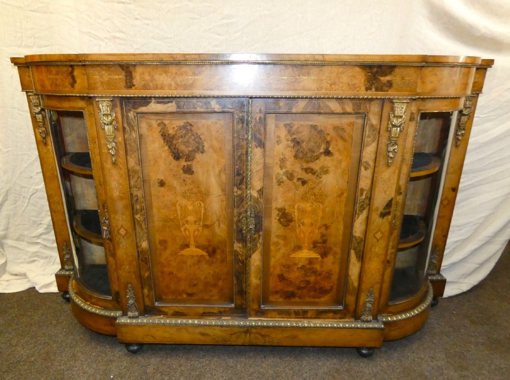 A Victorian burr walnut credenza featuring central wooden doors with marquetry urn motifs, flanked by curved glazed side compartments and gilt bronze mounts.