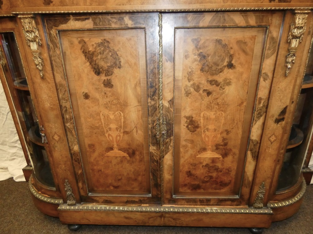 A Victorian burr walnut credenza featuring central wooden doors with marquetry urn motifs, flanked by curved glazed side compartments and gilt bronze mounts. View II