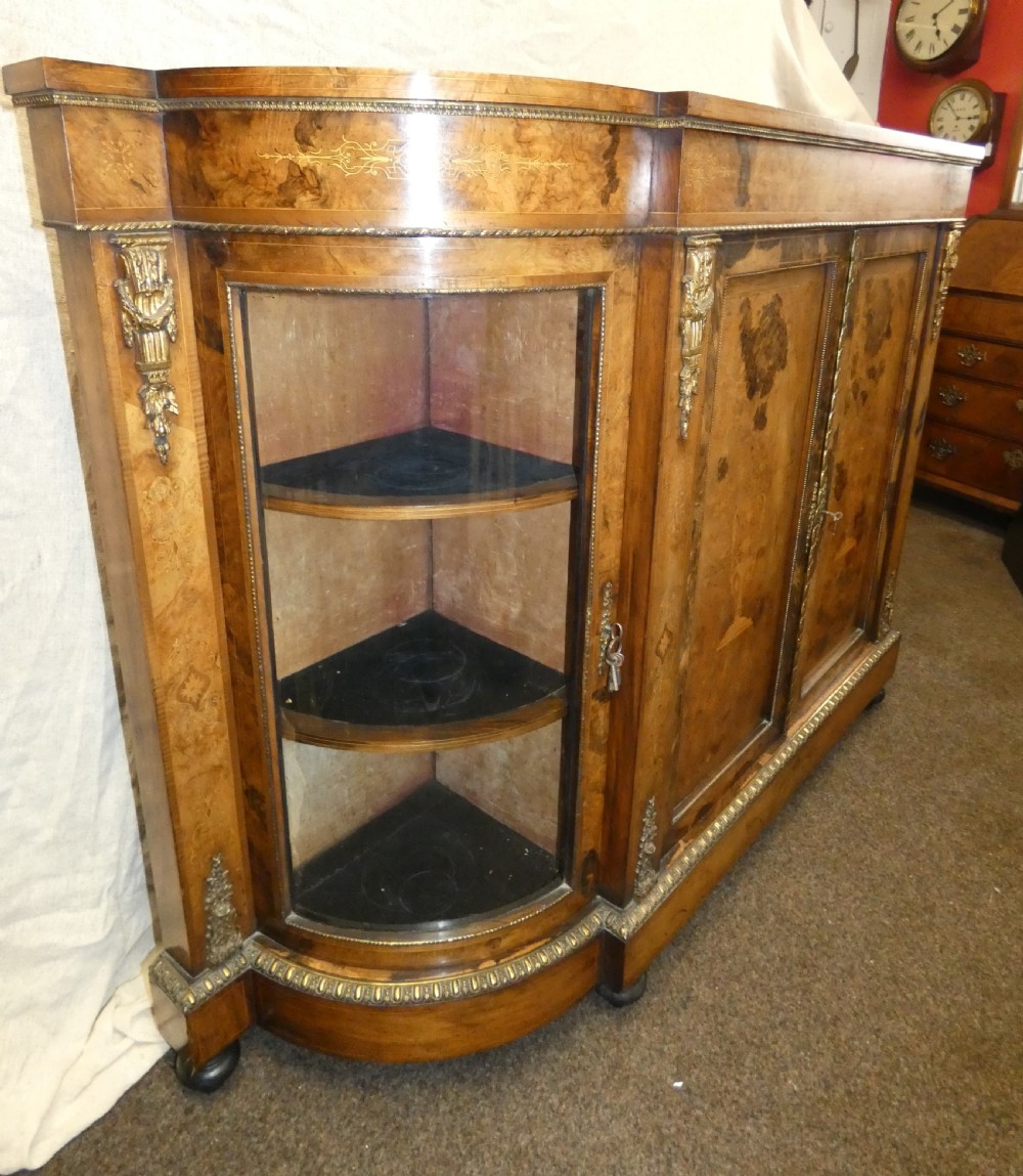 A Victorian burr walnut credenza featuring central wooden doors with marquetry urn motifs, flanked by curved glazed side compartments and gilt bronze mounts. View IV