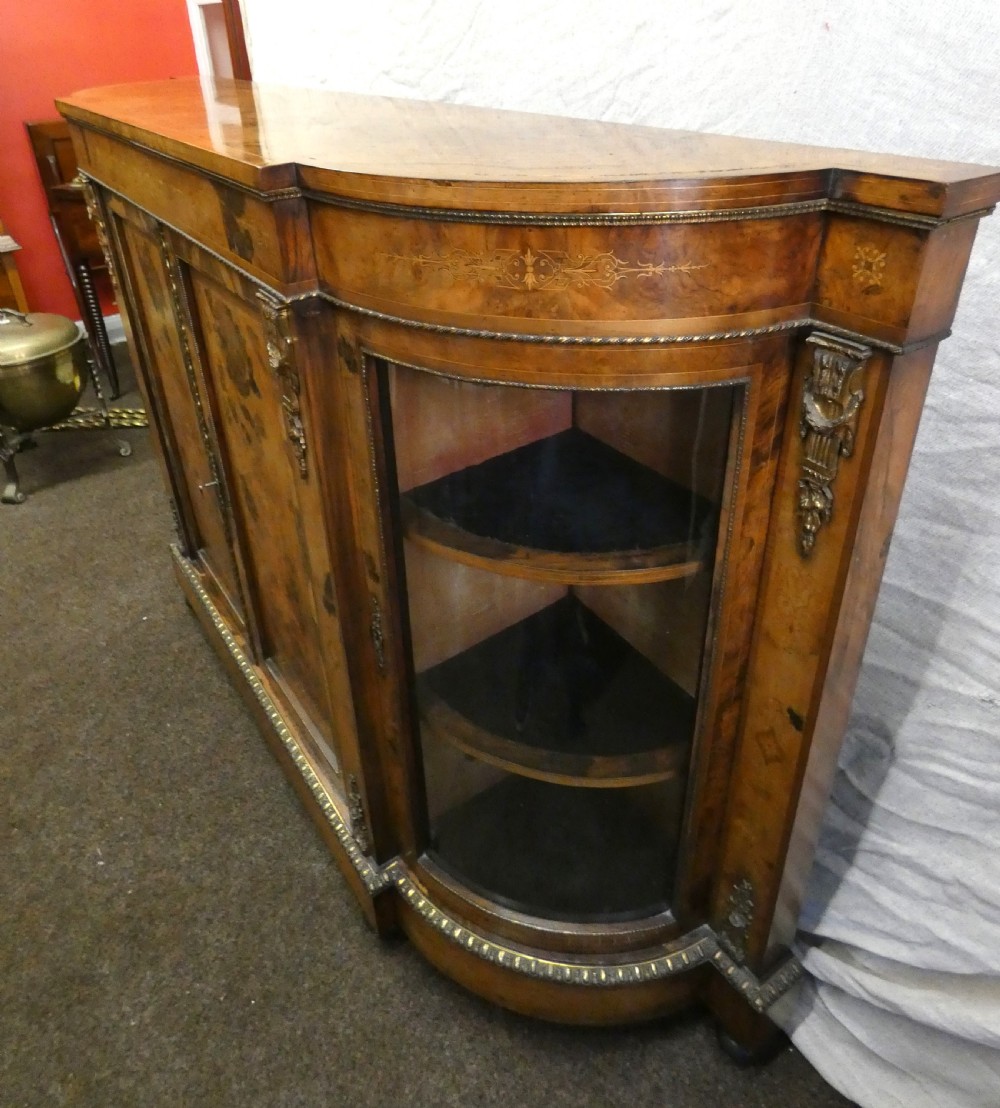 A Victorian burr walnut credenza featuring central wooden doors with marquetry urn motifs, flanked by curved glazed side compartments and gilt bronze mounts. View V