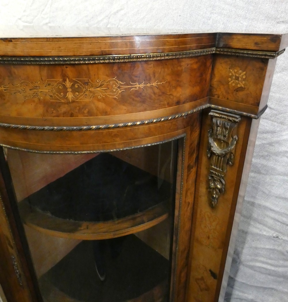 A Victorian burr walnut credenza featuring central wooden doors with marquetry urn motifs, flanked by curved glazed side compartments and gilt bronze mounts. View VI