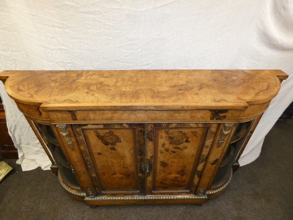 A Victorian burr walnut credenza featuring central wooden doors with marquetry urn motifs, flanked by curved glazed side compartments and gilt bronze mounts. View VII
