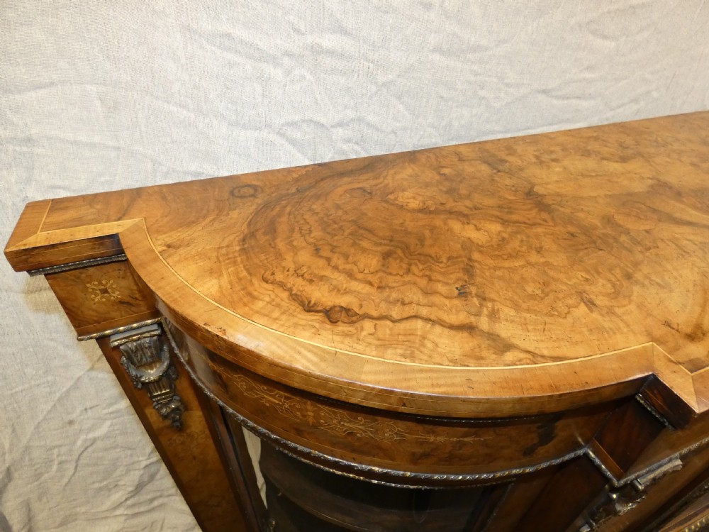 A Victorian burr walnut credenza featuring central wooden doors with marquetry urn motifs, flanked by curved glazed side compartments and gilt bronze mounts. View VIII