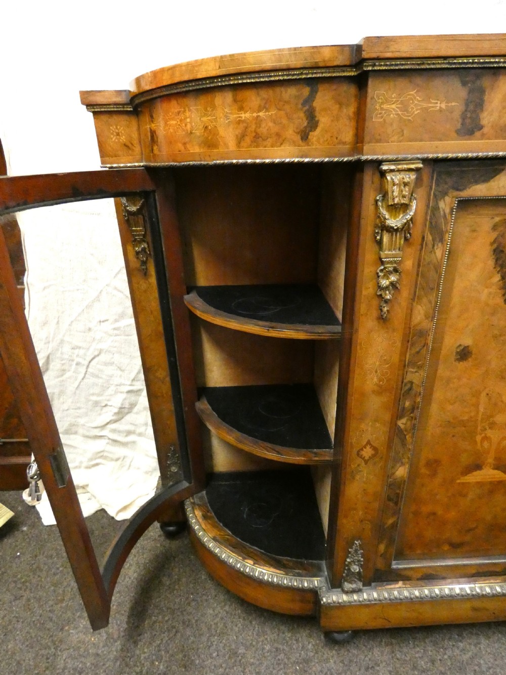 A Victorian burr walnut credenza featuring central wooden doors with marquetry urn motifs, flanked by curved glazed side compartments and gilt bronze mounts. View X