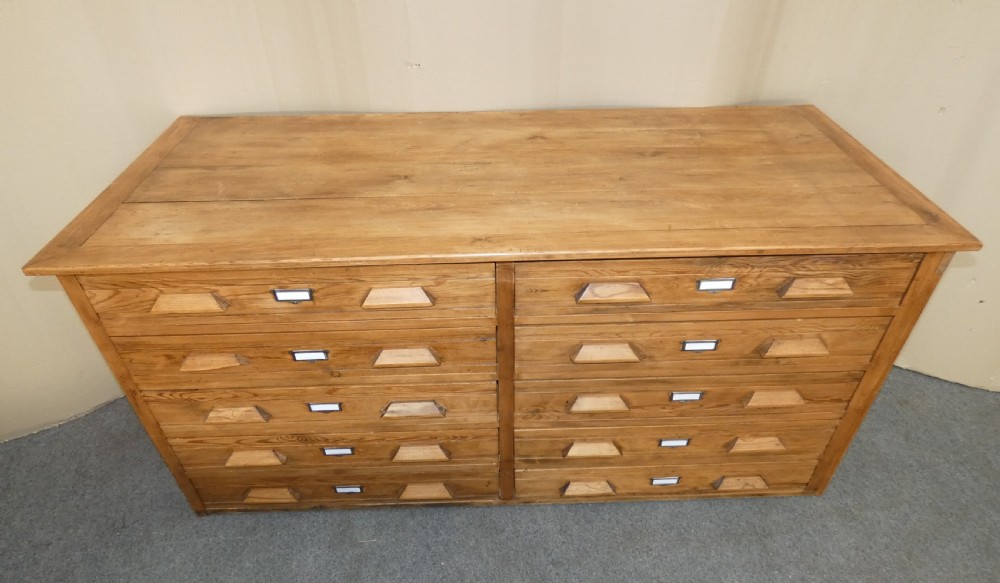 A wide pine cabinet featuring ten shallow drawers in two columns, each fitted with angular wooden handles and metal label holders. View II