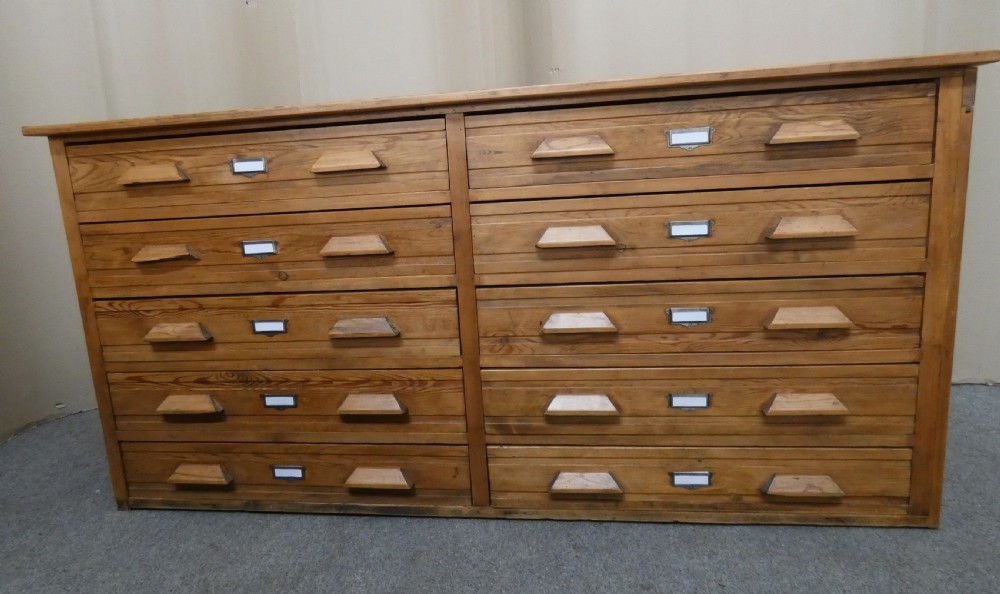 A wide pine cabinet featuring ten shallow drawers in two columns, each fitted with angular wooden handles and metal label holders. View III