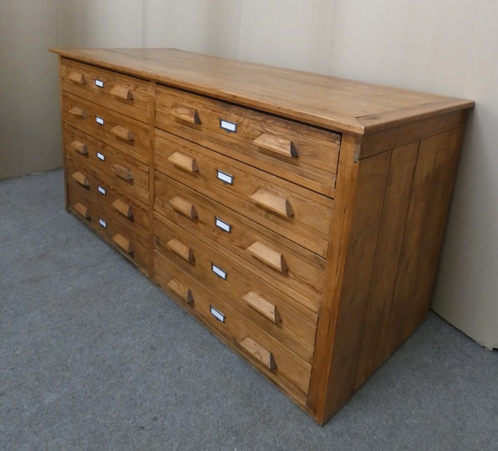 A wide pine cabinet featuring ten shallow drawers in two columns, each fitted with angular wooden handles and metal label holders. View IV