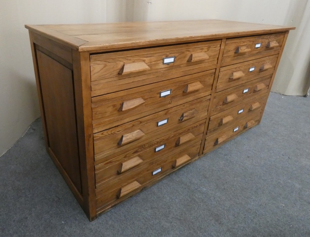 A wide pine cabinet featuring ten shallow drawers in two columns, each fitted with angular wooden handles and metal label holders. View V