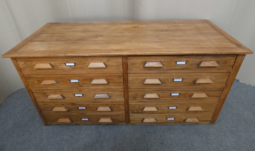 A wide pine cabinet featuring ten shallow drawers in two columns, each fitted with angular wooden handles and metal label holders. View VI