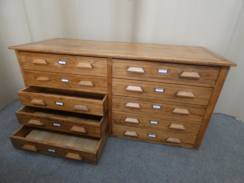 A wide pine cabinet featuring ten shallow drawers in two columns, each fitted with angular wooden handles and metal label holders. View VII