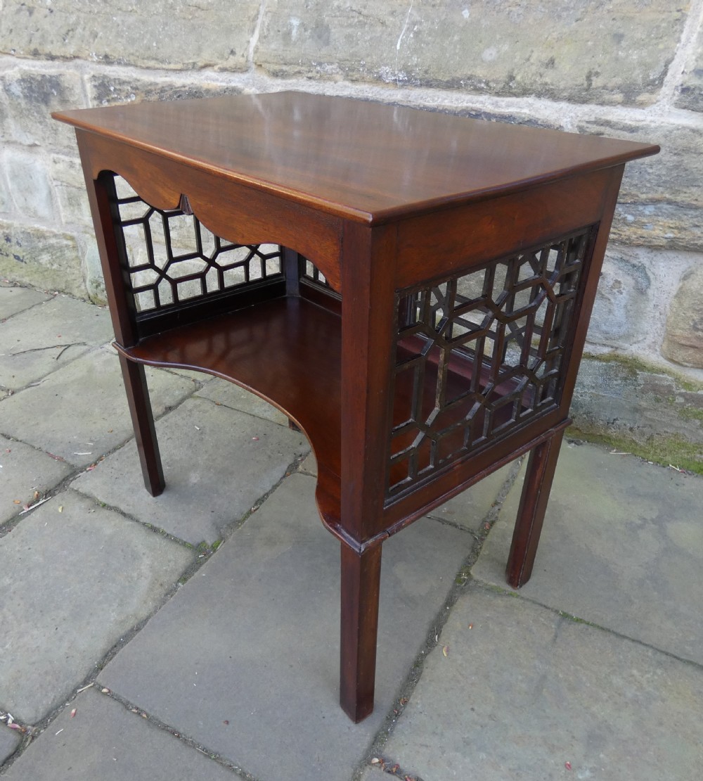 A dark mahogany side table featuring decorative geometric fretwork panels and a curved lower shelf.