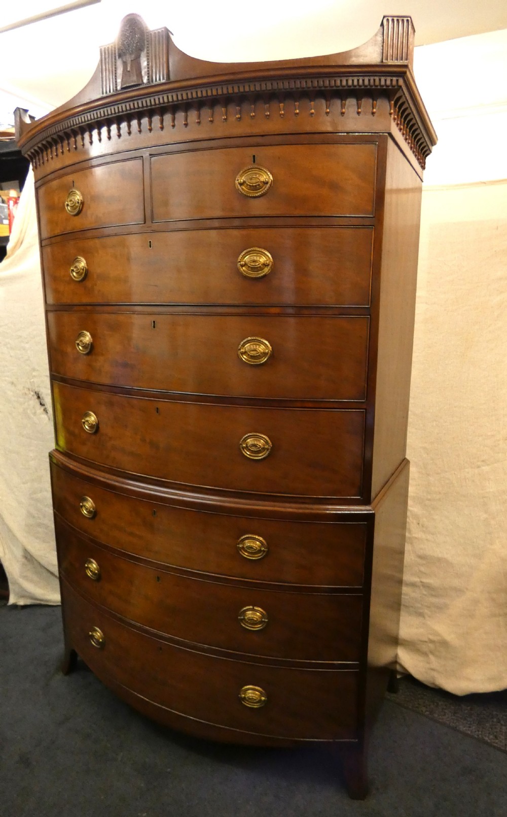 An antique bow-front mahogany chest on chest featuring graduated drawers, brass oval drop handles, and a carved pediment crown. View III