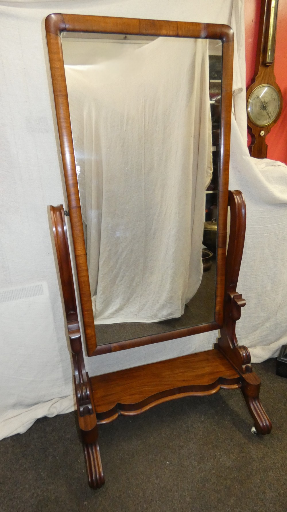 A freestanding Victorian mahogany cheval mirror featuring a rounded rectangular glass frame held by curved uprights above a serpentine base platform with splayed legs. View V