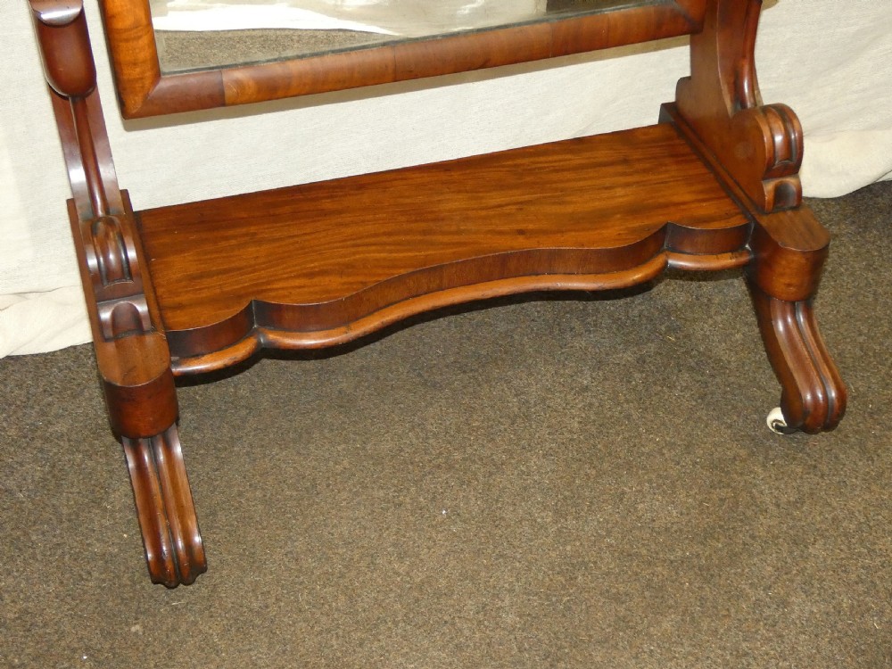 A freestanding Victorian mahogany cheval mirror featuring a rounded rectangular glass frame held by curved uprights above a serpentine base platform with splayed legs. View VI