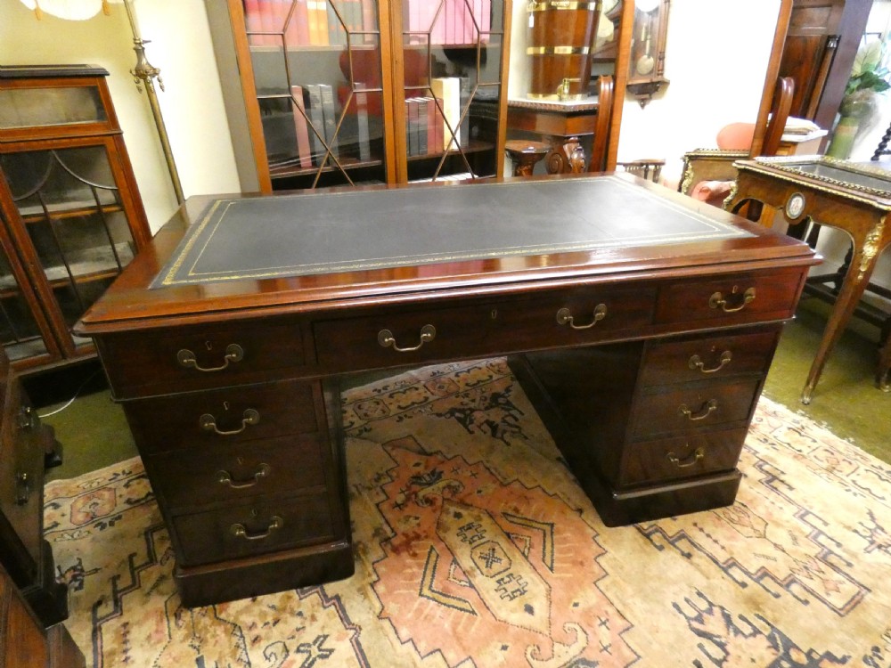 An antique mahogany partners desk featuring a dark leather writing surface, multiple pedestal drawers, and brass swan-neck handles.