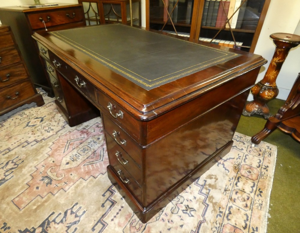 An antique mahogany partners desk featuring a dark leather writing surface, multiple pedestal drawers, and brass swan-neck handles. View V