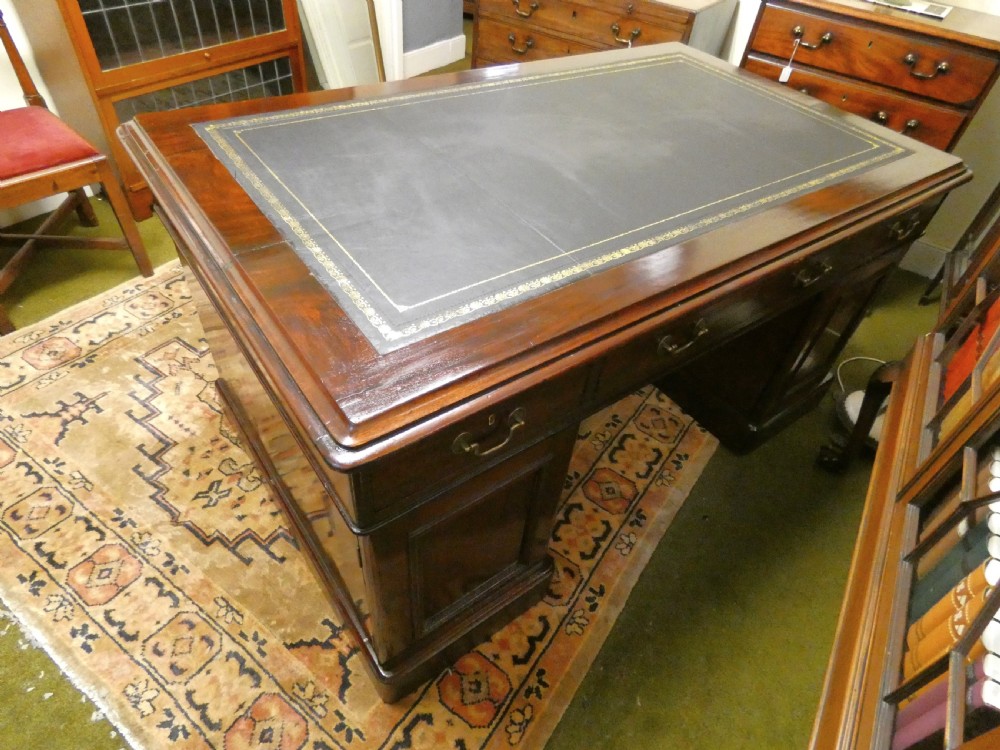 An antique mahogany partners desk featuring a dark leather writing surface, multiple pedestal drawers, and brass swan-neck handles. View VI