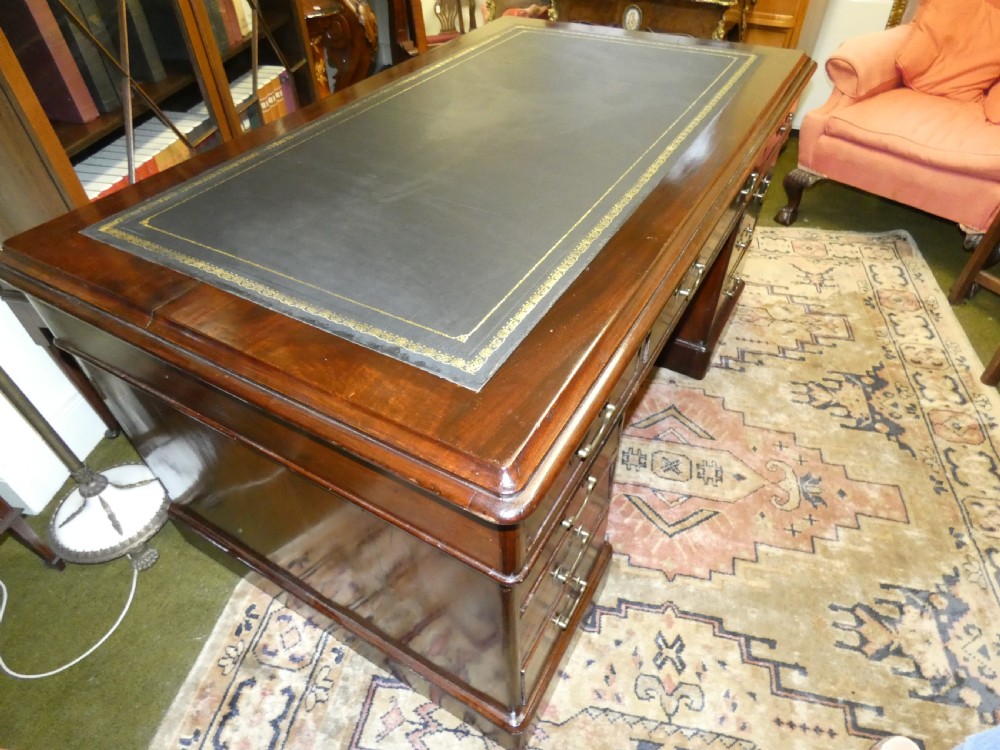 An antique mahogany partners desk featuring a dark leather writing surface, multiple pedestal drawers, and brass swan-neck handles. View IX