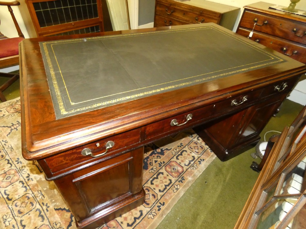 An antique mahogany partners desk featuring a dark leather writing surface, multiple pedestal drawers, and brass swan-neck handles. View X