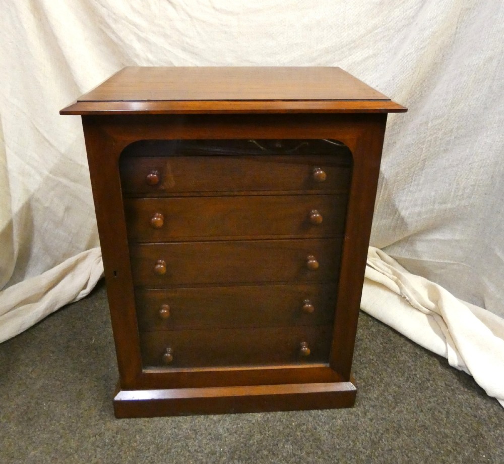 An antique warm brown mahogany specimen cabinet featuring five shallow drawers with wooden knob handles set behind a framed front on a plinth base.