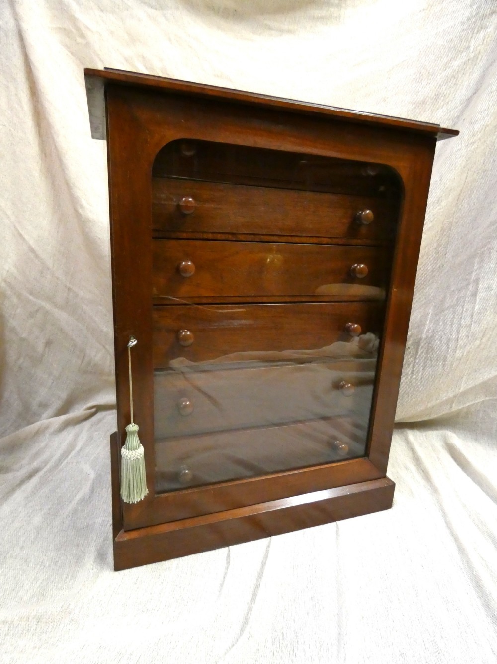 An antique warm brown mahogany specimen cabinet featuring five shallow drawers with wooden knob handles set behind a framed front on a plinth base. View II