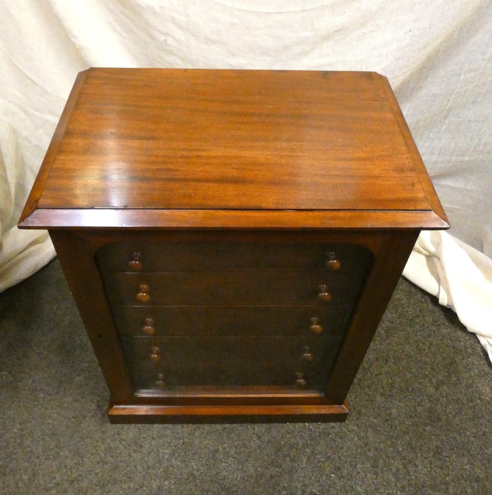 An antique warm brown mahogany specimen cabinet featuring five shallow drawers with wooden knob handles set behind a framed front on a plinth base. View IV