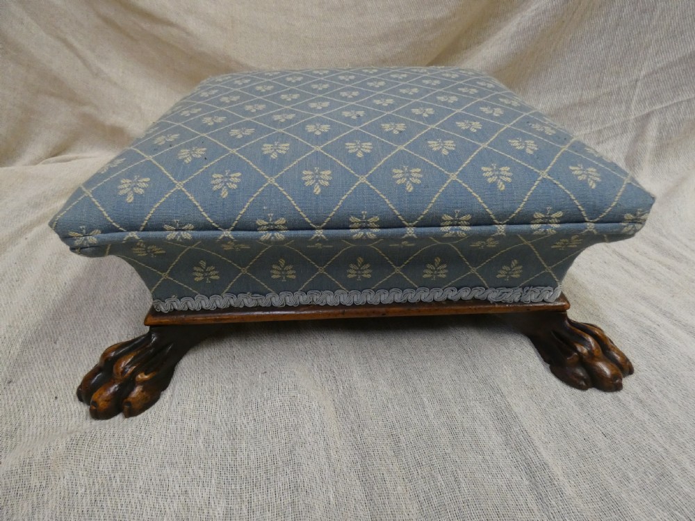 A low square upholstered footstool featuring light blue patterned fabric, decorative braid trim, and dark carved timber claw feet. View II