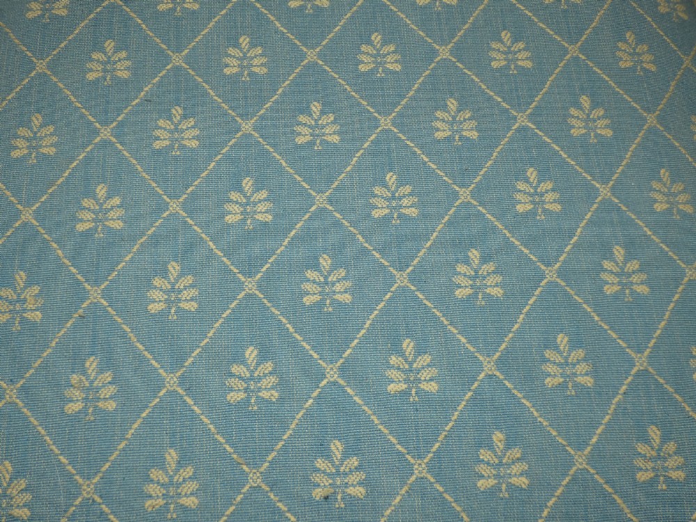 A low square upholstered footstool featuring light blue patterned fabric, decorative braid trim, and dark carved timber claw feet. View VI