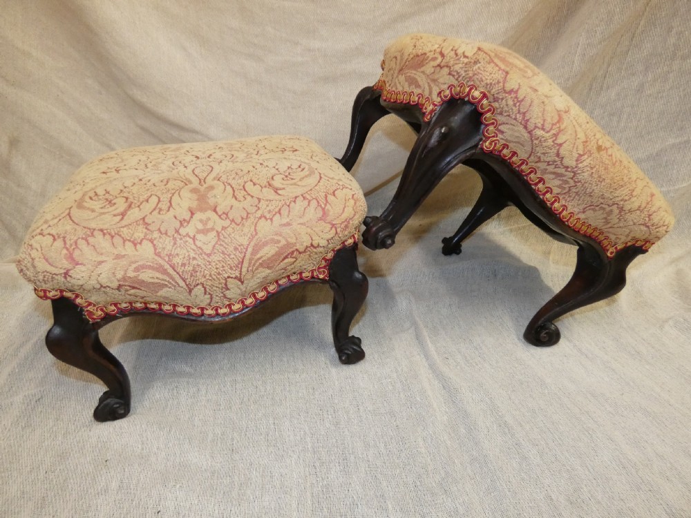 A pair of low antique footstools featuring carved dark wood cabriole legs and gold damask pattern fabric upholstery. View II