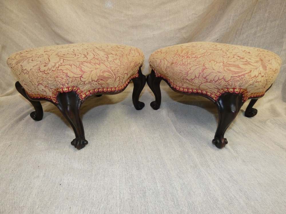 A pair of low antique footstools featuring carved dark wood cabriole legs and gold damask pattern fabric upholstery. View III