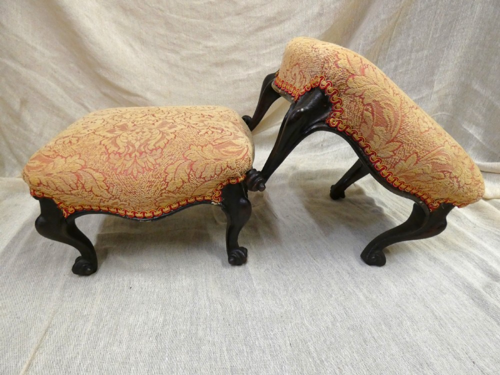 A pair of low antique footstools featuring carved dark wood cabriole legs and gold damask pattern fabric upholstery. View VI
