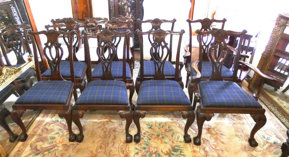 A set of eight dark mahogany Chippendale style dining chairs featuring carved pierced splats, cabriole legs with ball and claw feet, and blue tartan upholstered seats.
