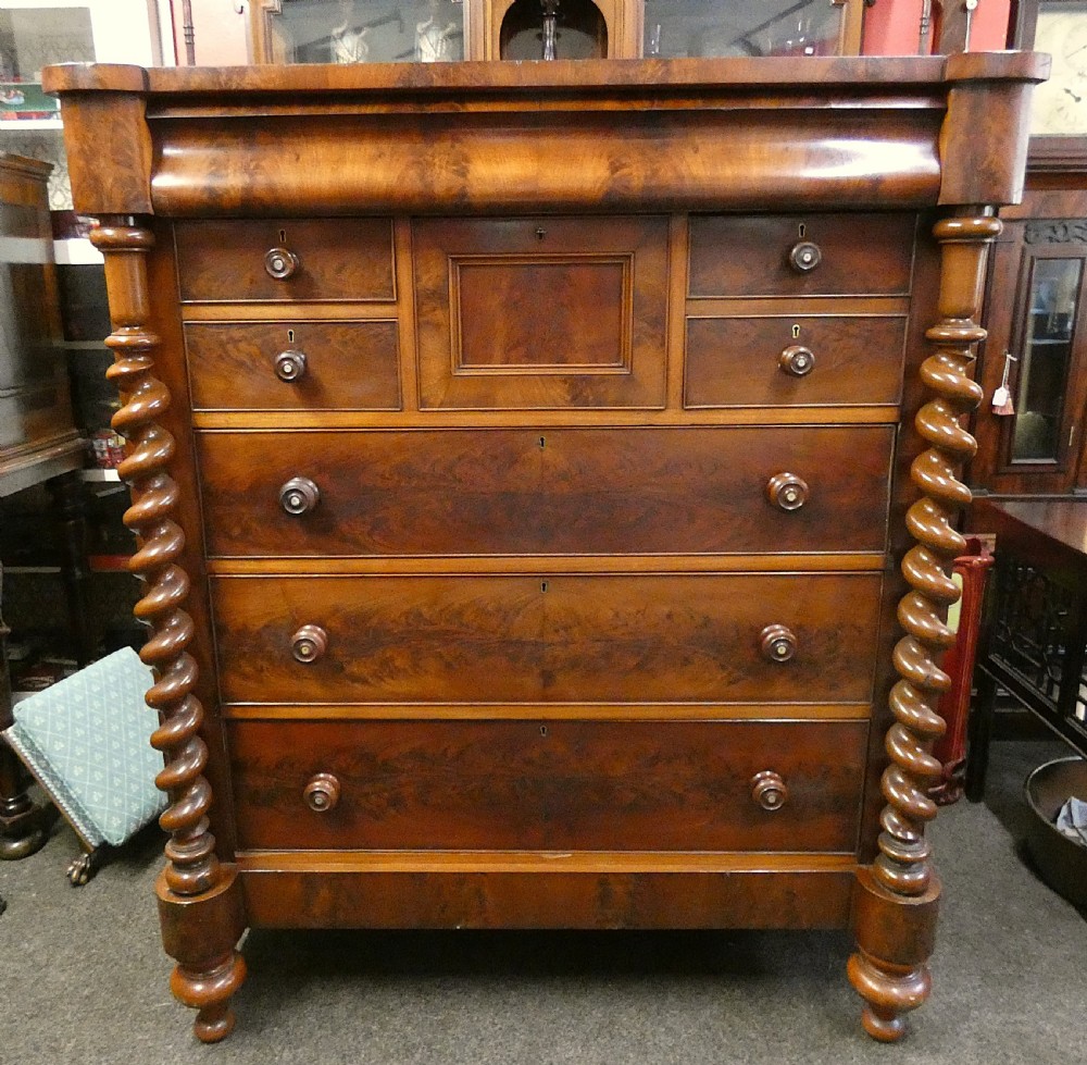 A tall Victorian flame mahogany Scotch chest of drawers featuring spiral barley twist side columns, a central square drawer flanked by smaller drawers, and three long graduated drawers below.