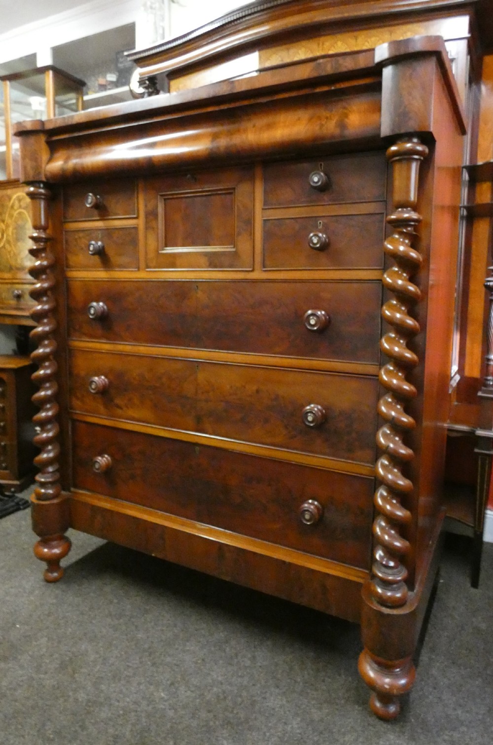 A tall Victorian flame mahogany Scotch chest of drawers featuring spiral barley twist side columns, a central square drawer flanked by smaller drawers, and three long graduated drawers below. View IV