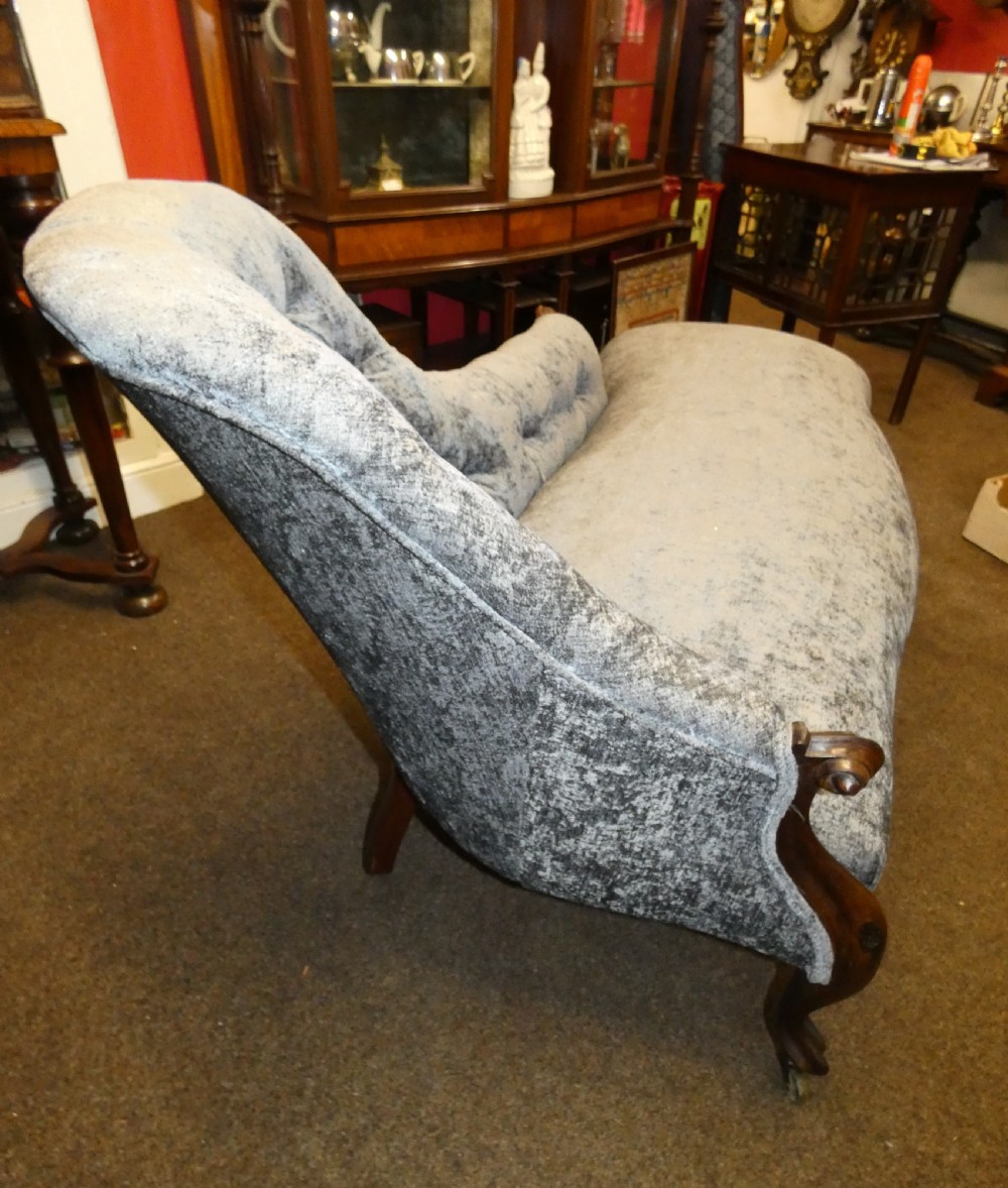 A Victorian-style chaise longue upholstered in textured grey fabric featuring a deep button-tufted asymmetrical backrest and carved wooden cabriole legs on brass castors. View V