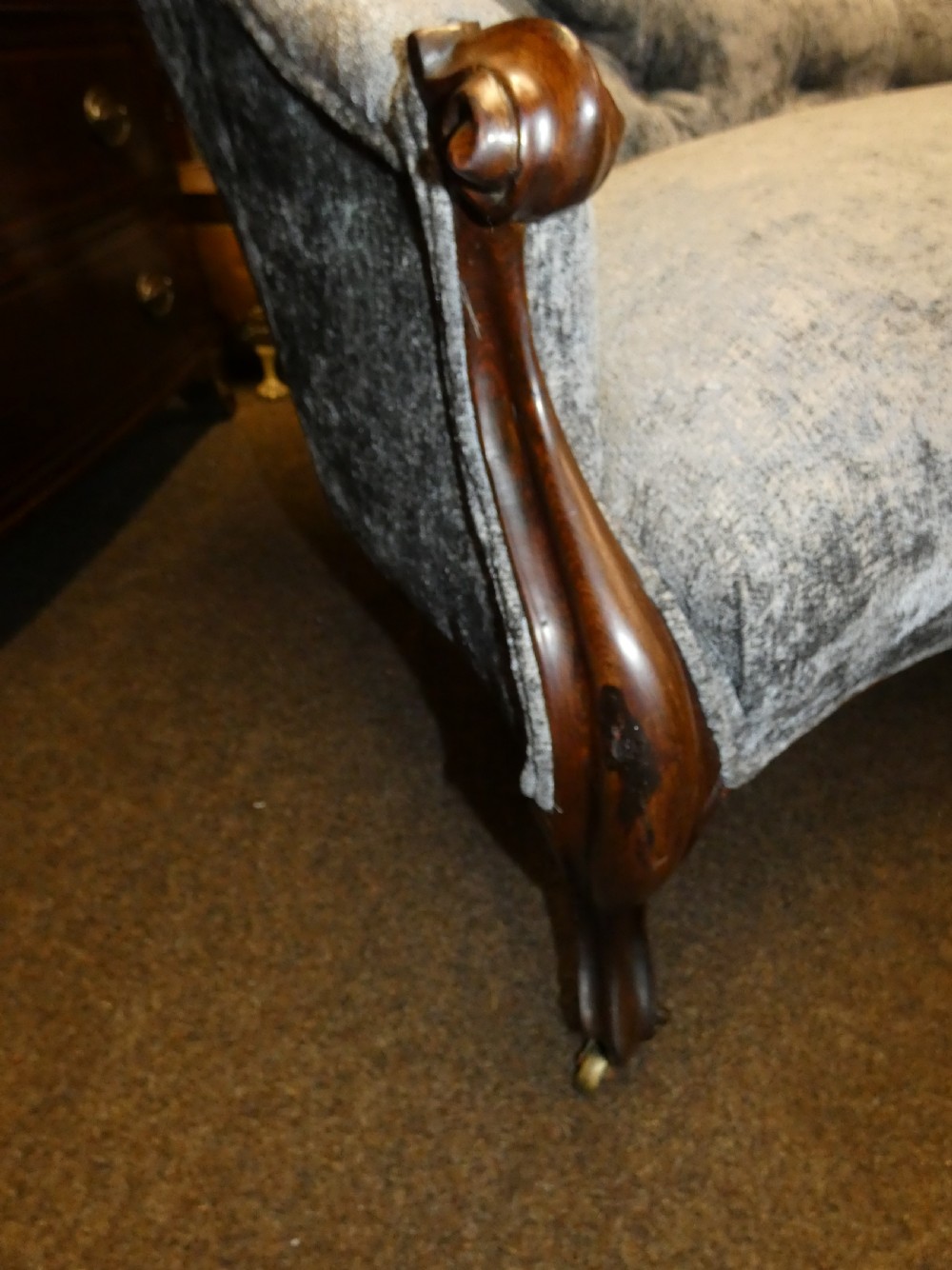 A Victorian-style chaise longue upholstered in textured grey fabric featuring a deep button-tufted asymmetrical backrest and carved wooden cabriole legs on brass castors. View VII