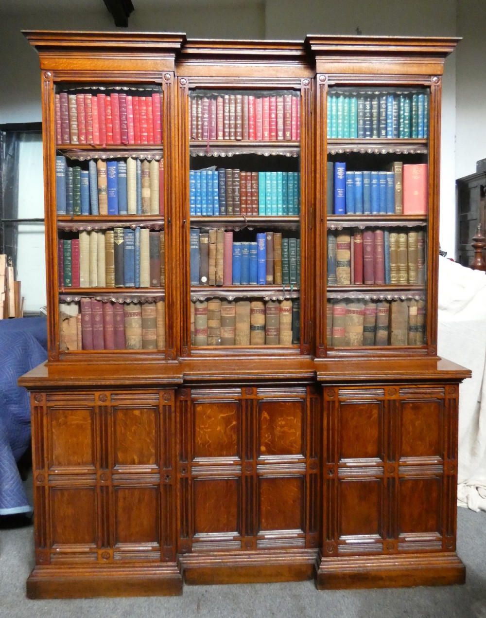 A large three-section antique oak bookcase featuring glazed upper doors above panelled lower cupboards. View II