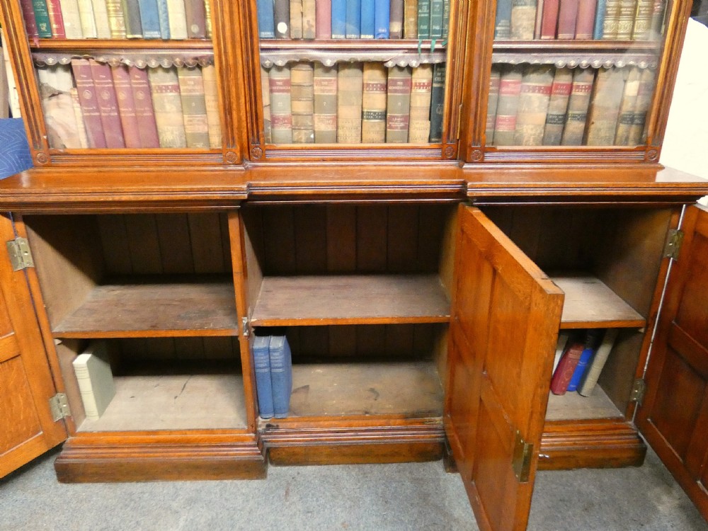 A large three-section antique oak bookcase featuring glazed upper doors above panelled lower cupboards. View VII
