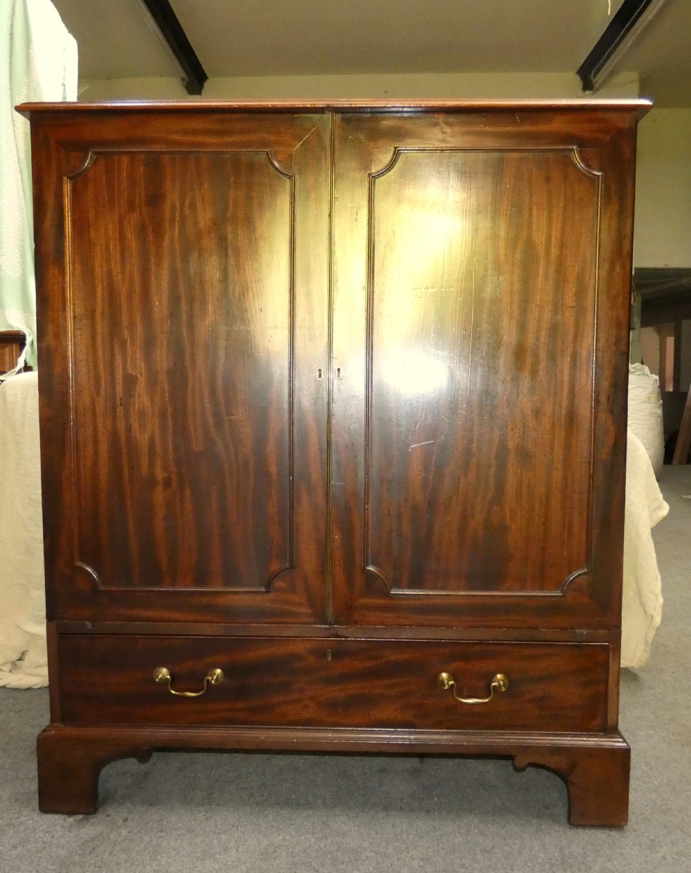 A Georgian mahogany dwarf press cupboard featuring twin panelled doors over a single drawer with brass handles. View V