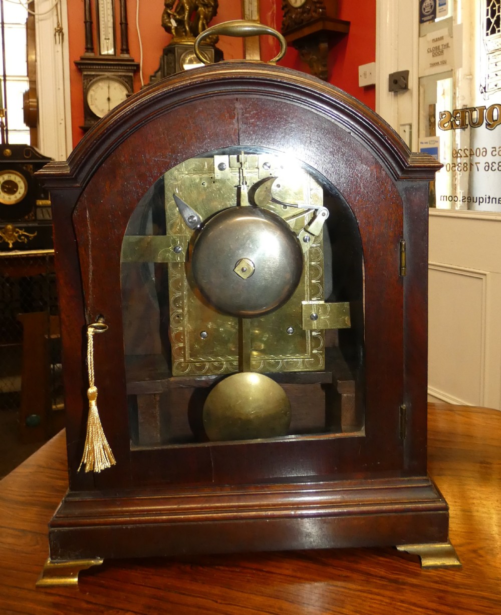 An antique dark mahogany bracket clock featuring an arched top with a brass carrying handle, a circular white dial signed Thos. Howard London, and brass fish-scale grilles. View VIII