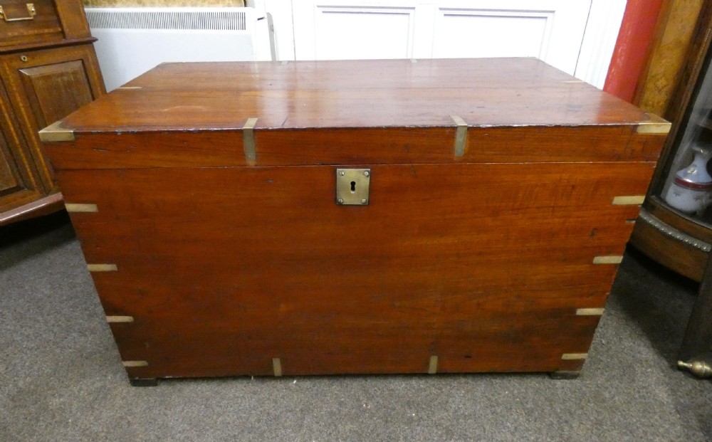 A rectangular warm brown mahogany military trunk featuring flush brass corner brackets, brass bindings, and a central keyhole escutcheon.