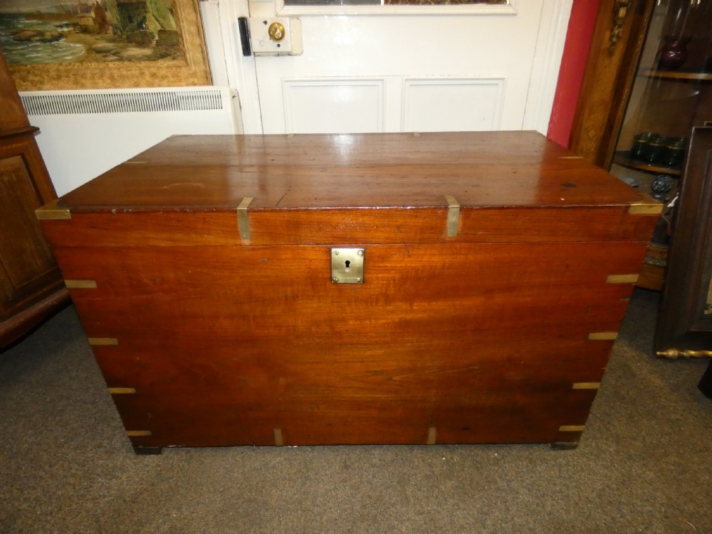 A rectangular warm brown mahogany military trunk featuring flush brass corner brackets, brass bindings, and a central keyhole escutcheon. View V