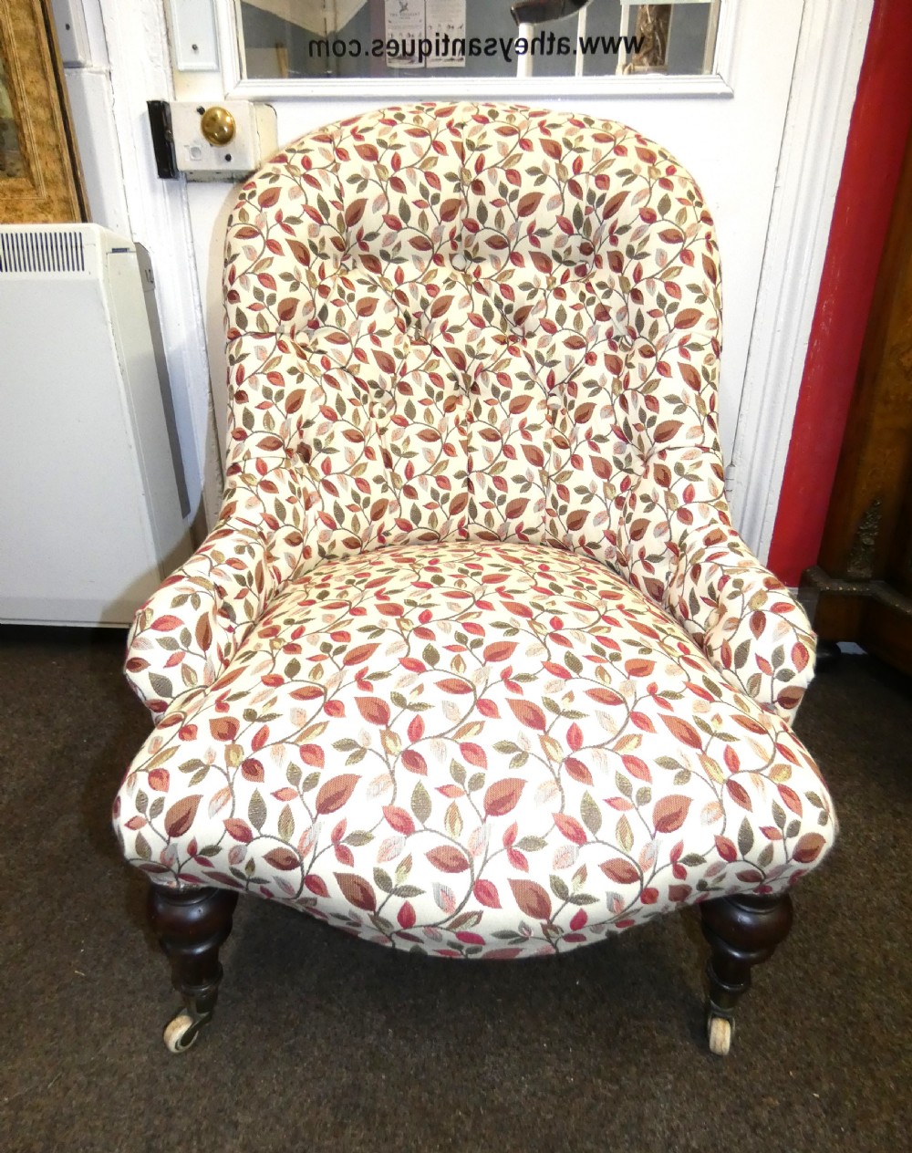 A Victorian low-seated button-back nursing chair featuring a leaf-patterned upholstery fabric and dark turned timber front legs with castors.
