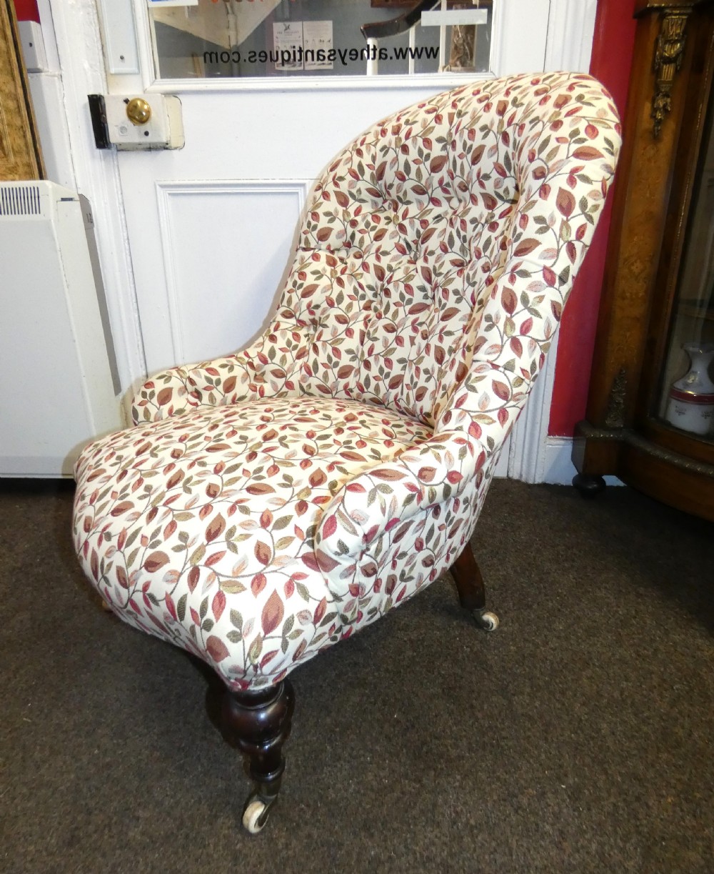 A Victorian low-seated button-back nursing chair featuring a leaf-patterned upholstery fabric and dark turned timber front legs with castors. View II