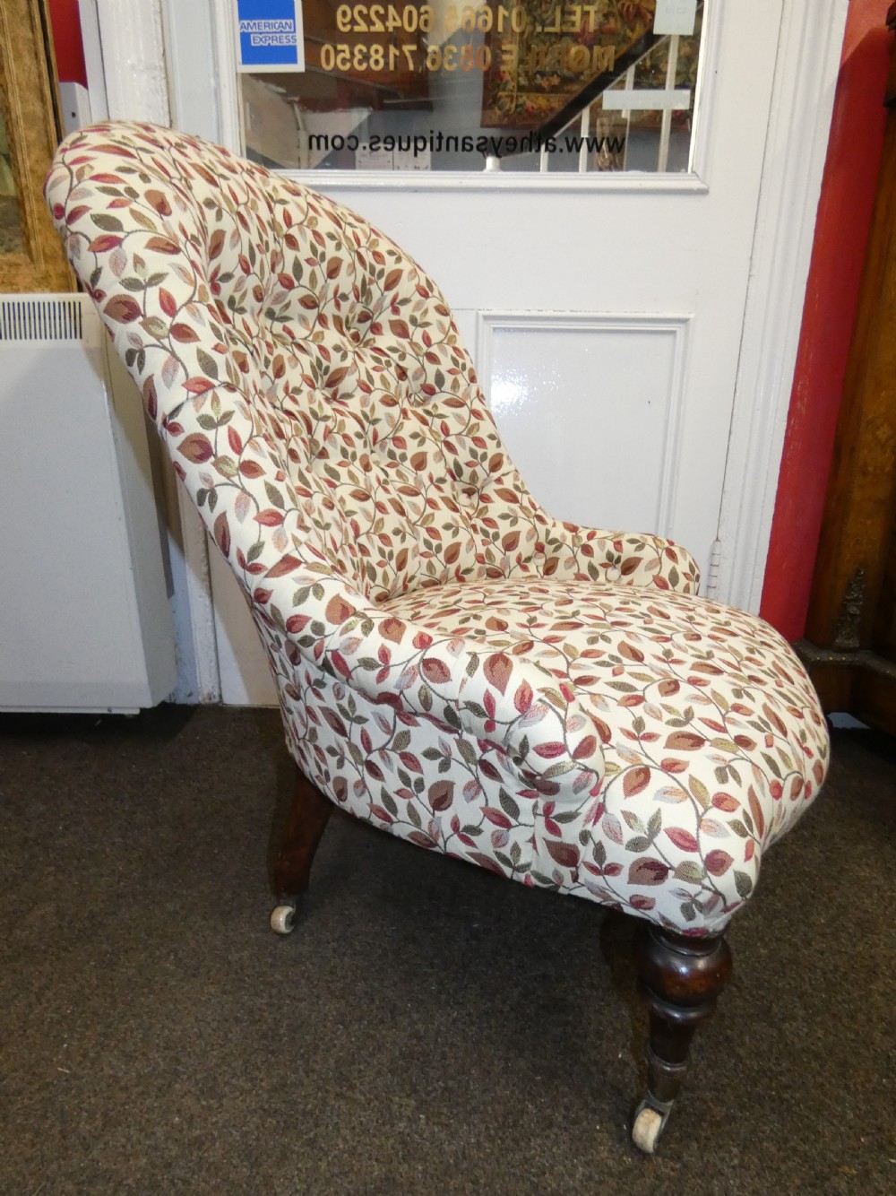 A Victorian low-seated button-back nursing chair featuring a leaf-patterned upholstery fabric and dark turned timber front legs with castors. View III