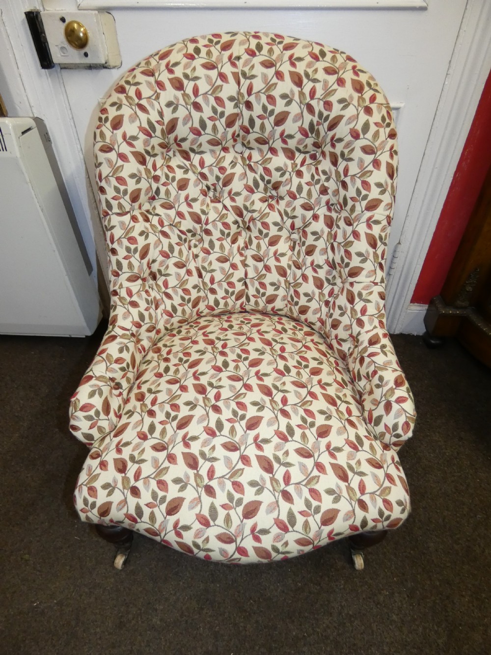 A Victorian low-seated button-back nursing chair featuring a leaf-patterned upholstery fabric and dark turned timber front legs with castors. View IV