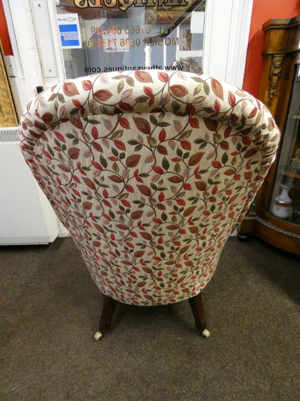 A Victorian low-seated button-back nursing chair featuring a leaf-patterned upholstery fabric and dark turned timber front legs with castors. View V