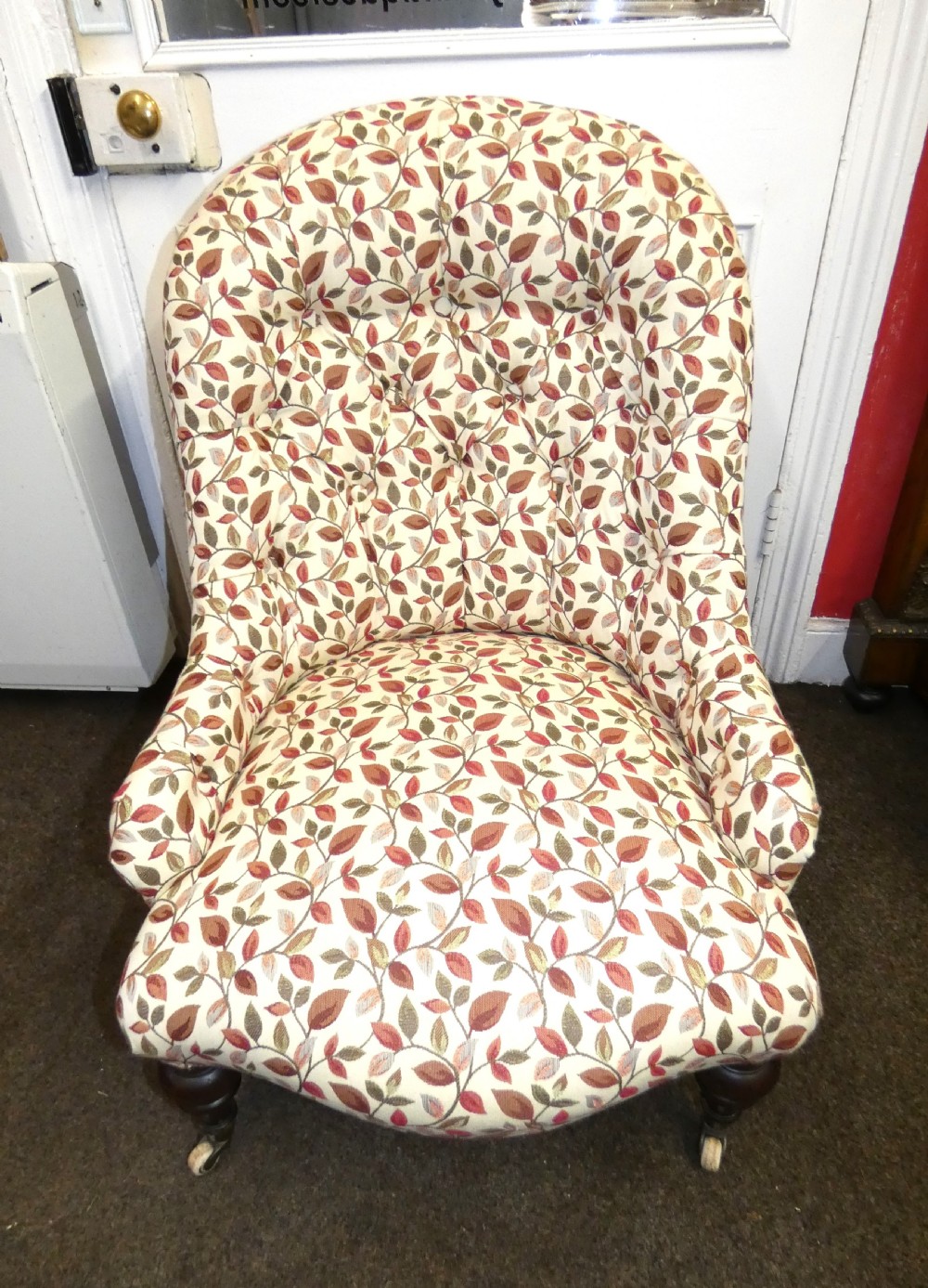 A Victorian low-seated button-back nursing chair featuring a leaf-patterned upholstery fabric and dark turned timber front legs with castors. View VI